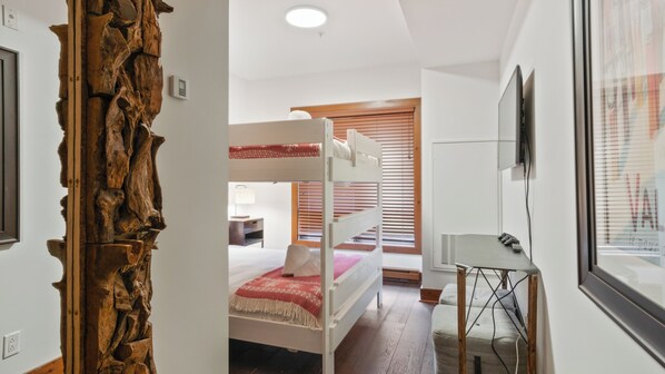 A room with bunk beds, a desk, and a wooden wall feature.