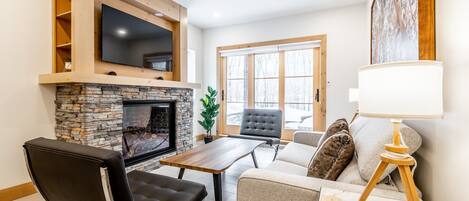 Una sala de estar moderna con chimenea de piedra, un televisor de pantalla plana montado sobre ella y un espacio de estar cómodo con sofá y sillones.