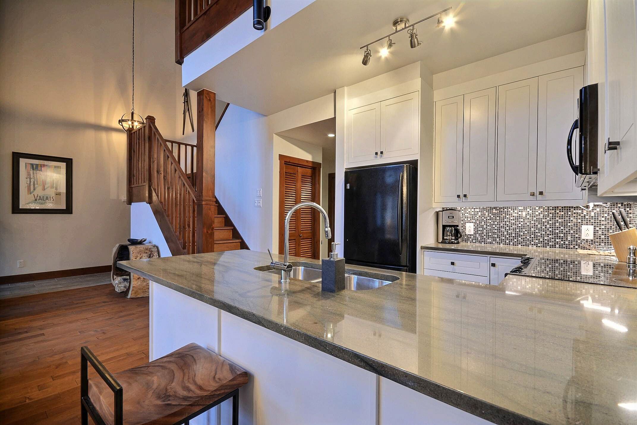Una cocina moderna con una isla grande, armarios blancos y un refrigerador negro.