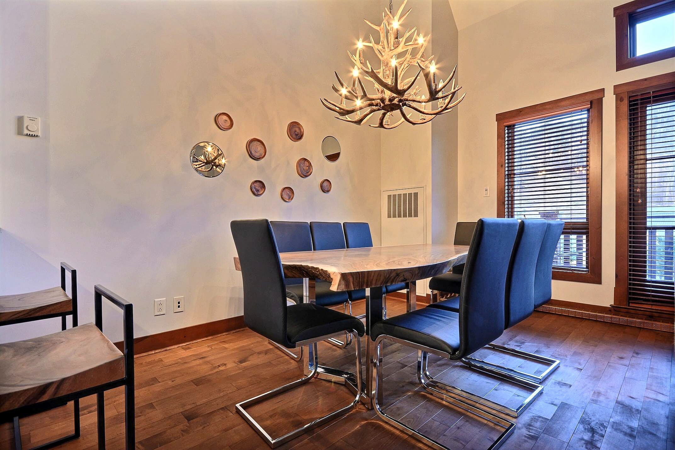 Un comedor con mesa de madera, sillas tapizadas en azul, una araña y detalles decorativos en la pared.