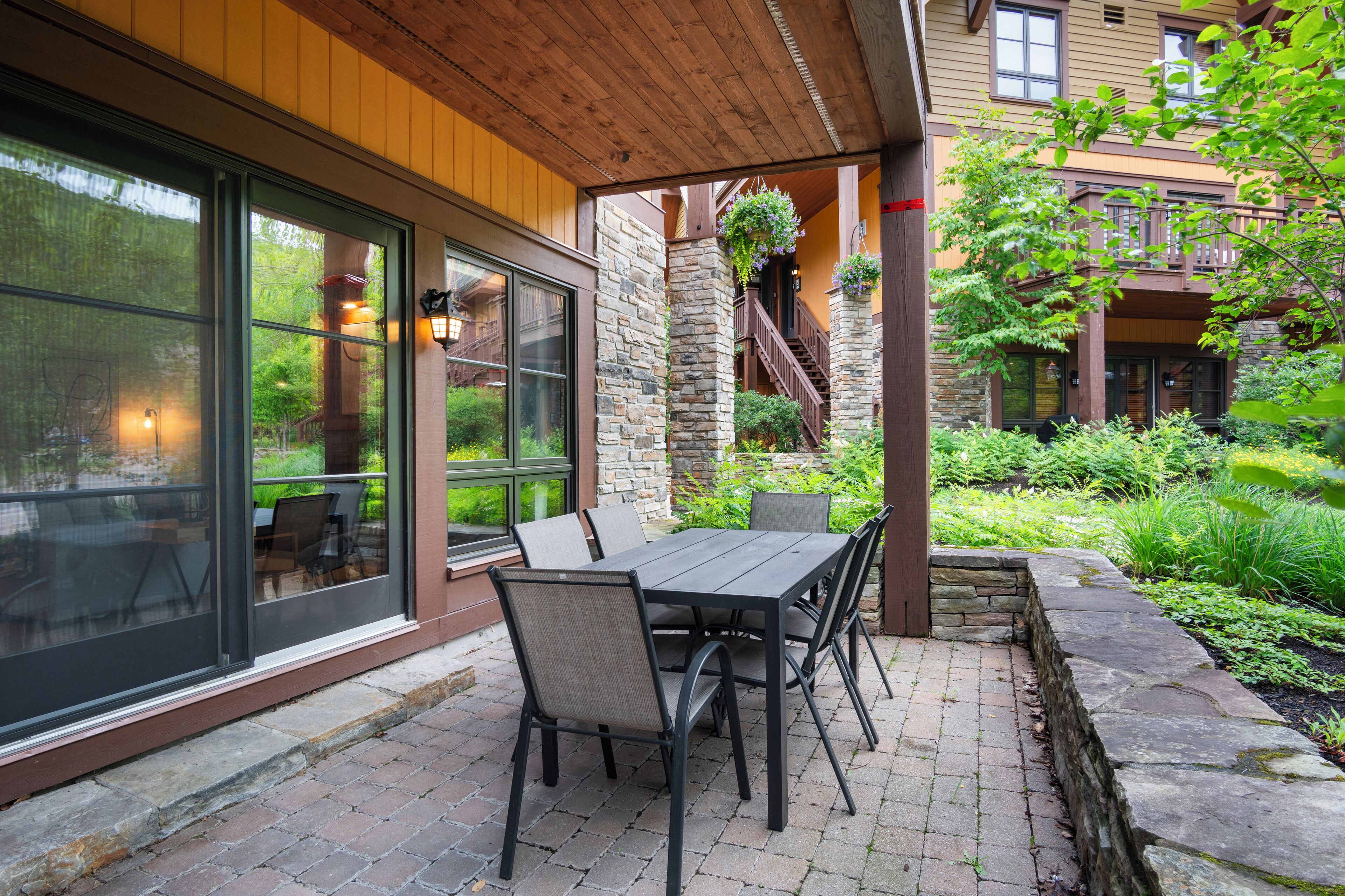 A patio with a table and chairs, a stone wall, and a staircase leading to a balcony.