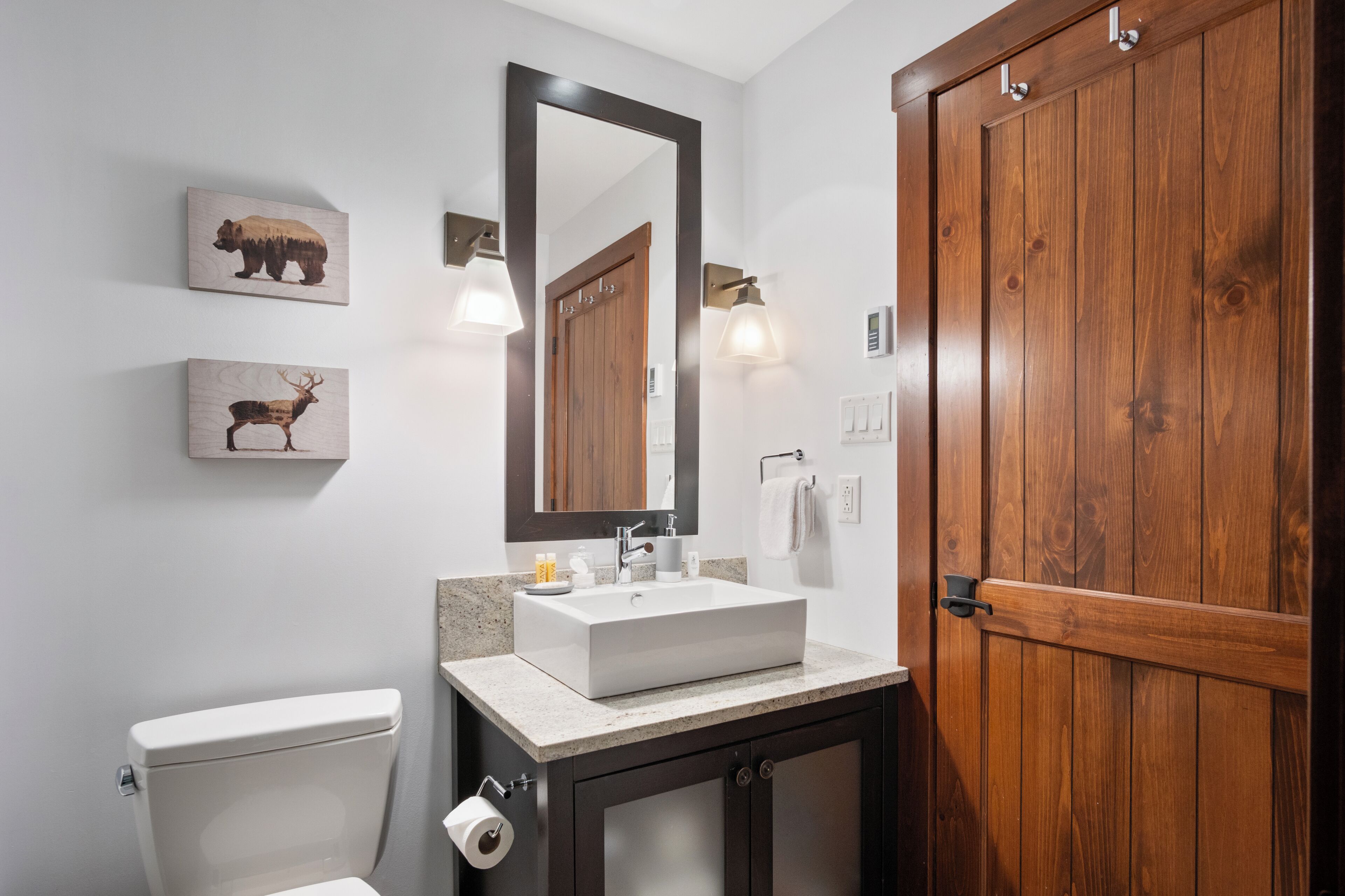 A bathroom with a wooden door, a white sink, a mirror, and two wall-mounted light fixtures.