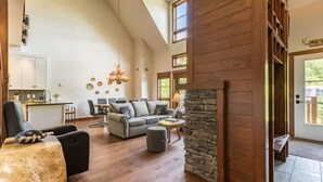 A spacious living area with a fireplace, wooden flooring, and a dining area with a kitchen in the background.