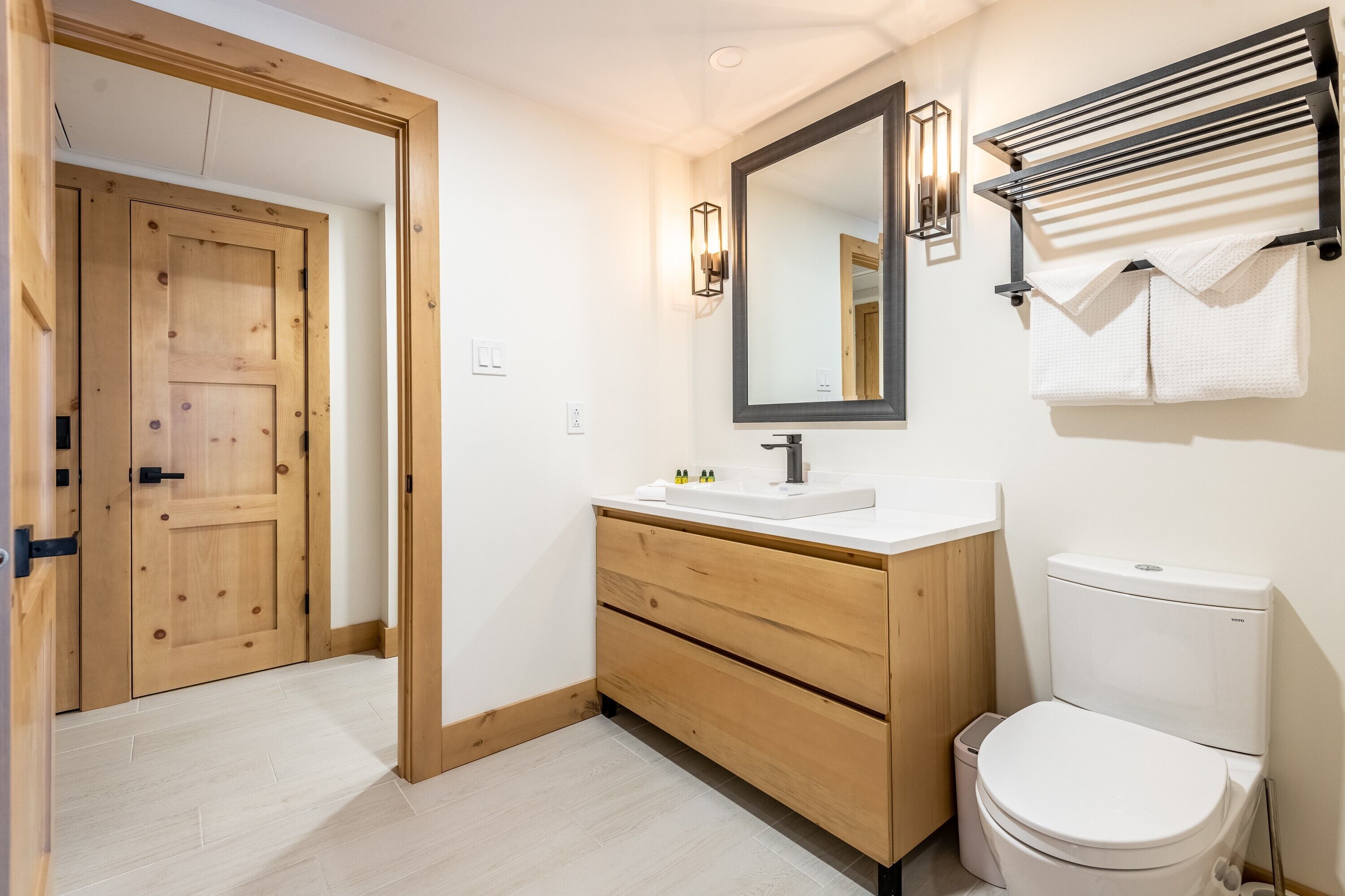 Un baño con puerta de madera, un lavabo blanco, un espejo y un perchero para toallas.