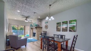 A dining area with a wooden table and chairs, a stone fireplace, and artwork on the wall. - CW C107 Spritzen Haus (New Braunfels)