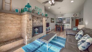 A living room with a stone fireplace, a ceiling fan, and a blue rug. - CW C107 Spritzen Haus (New Braunfels)
