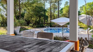 A wooden table and chairs in a covered outdoor area with a pool and lounge chairs in the background. - Villa 97 with private pool by Trip2Portugal (Alcácer do Sal)