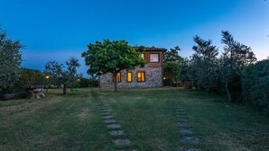 A stone house with a tree in front, surrounded by a well-maintained lawn and stone steps leading to the entrance. - Poggio Medei 10, Emma Villas (Città della Pieve)