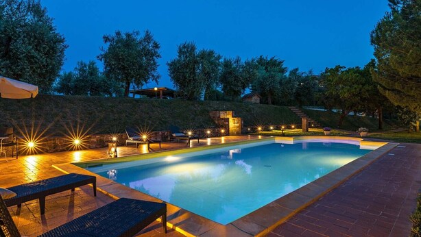 A swimming pool with a surrounding deck, outdoor seating, and a stone structure in the background. - Poggio Medei 10, Emma Villas (Città della Pieve)
