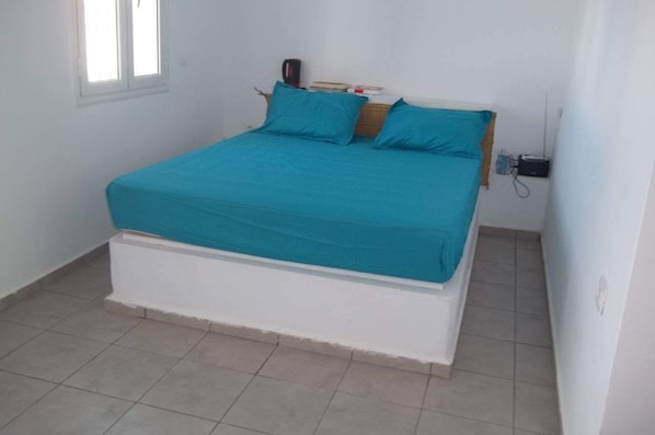 A single-bed room with a teal bedspread, white headboard, and a small bedside table.