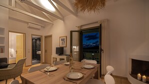 A dining room with a long wooden table set for four, white chairs, a television, and a fireplace.