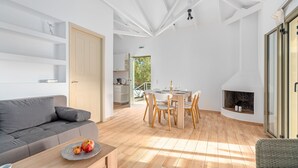 A modern living room with a sofa, dining table, and chairs. There is a fireplace and a view of the outdoors.
