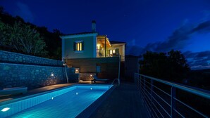 A two-story house with a swimming pool, stone wall, and a balcony with a railing.
