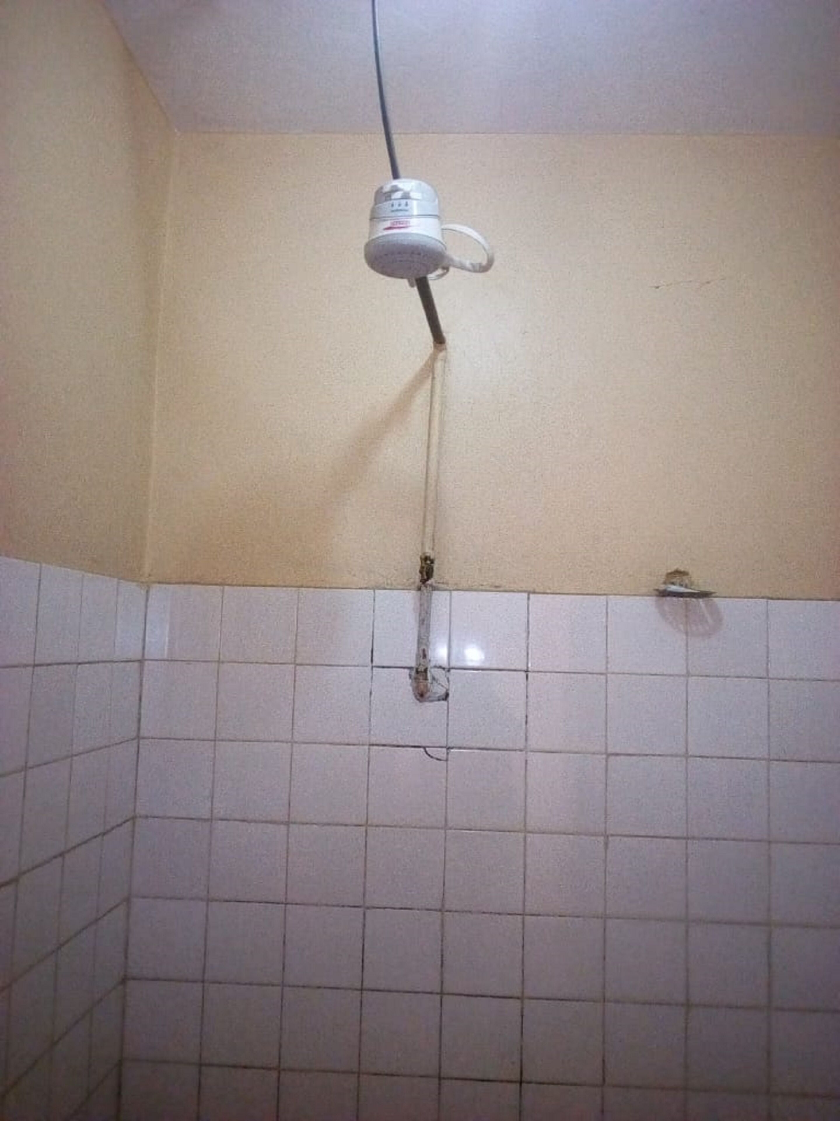A bathroom with white tiled walls, a shower area, and a hanging light fixture.