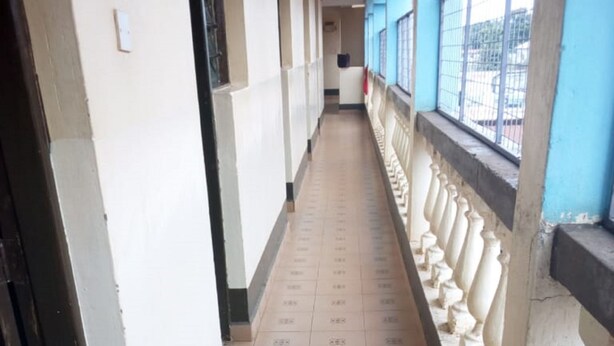 A corridor with tiled flooring, a blue railing, and a white wall with a window. - Mombasa Guest House (Kerugoya)