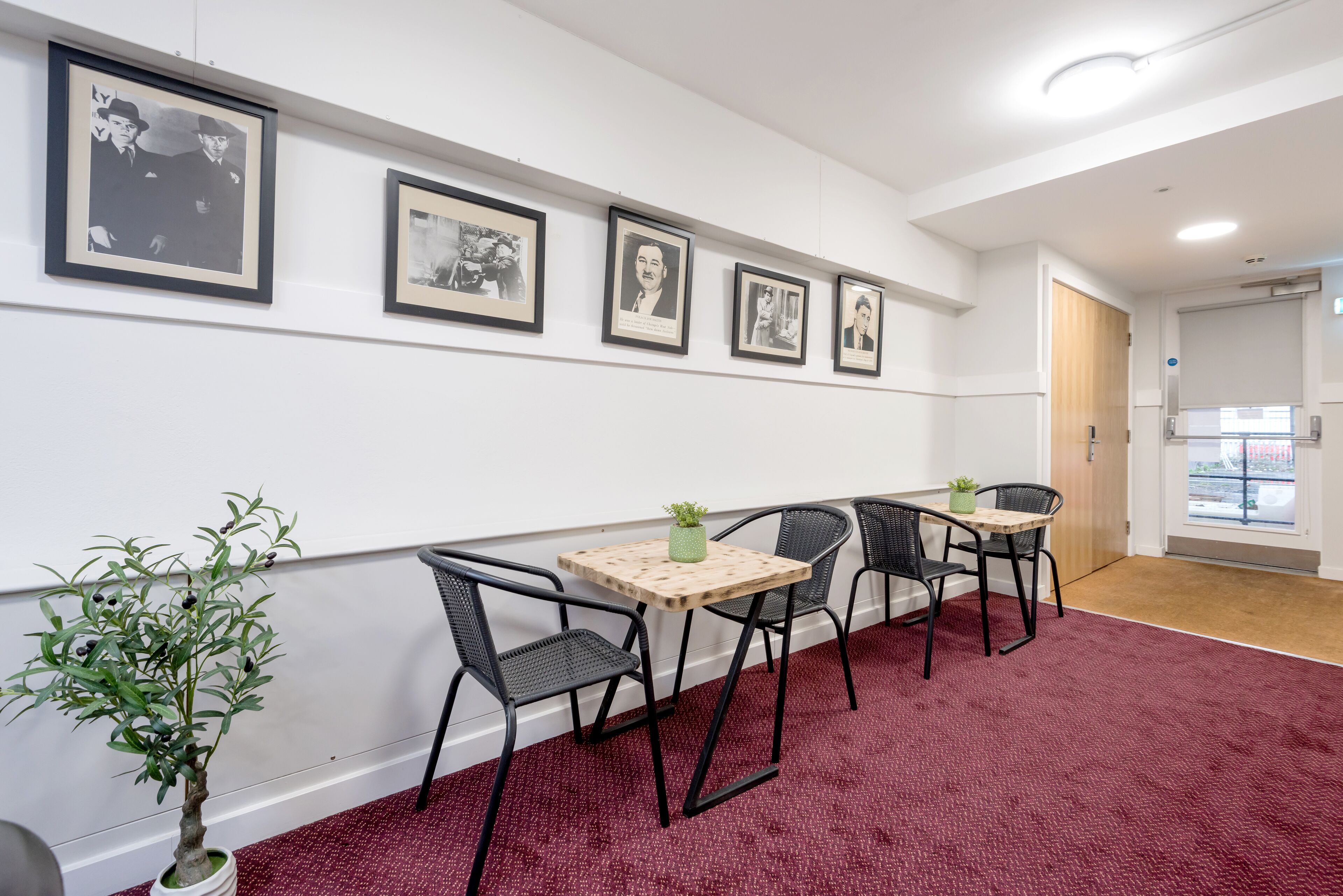 A hallway with framed pictures on the wall, a small table with a plant, and four chairs.