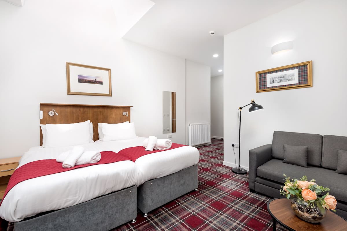 Une chambre d’hôtel avec un lit, un canapé, une lampe sur pied et un vase de fleurs.