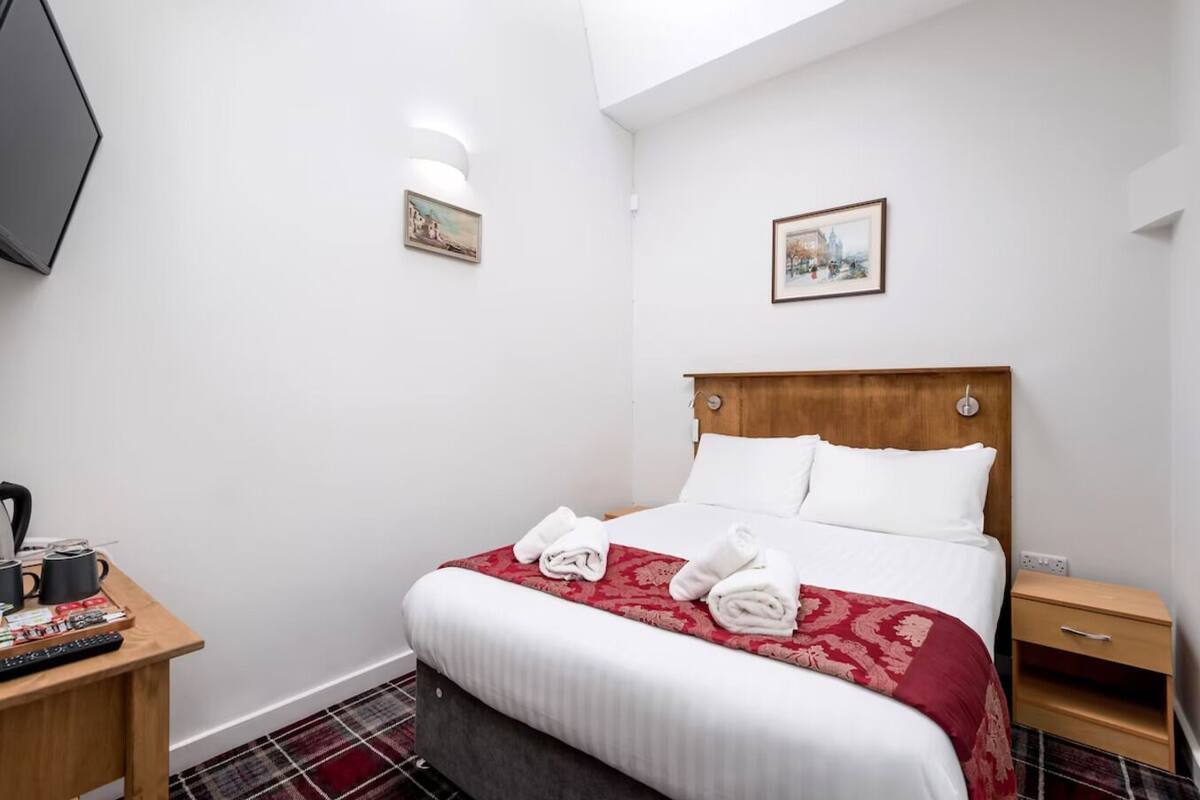 Une chambre d’hôtel comprenant un lit, une table de chevet avec une télécommande, une commode et un téléviseur fixé au mur.
