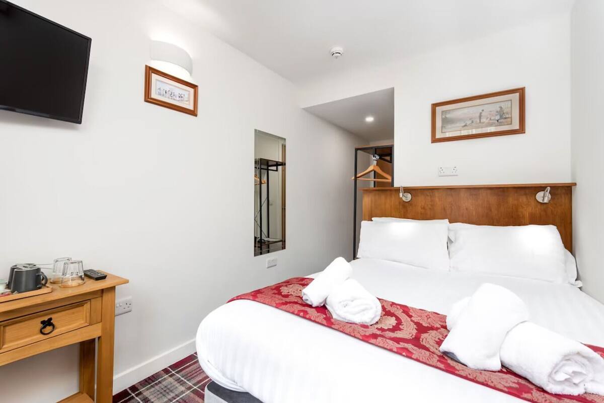 Une chambre d’hôtel avec un lit, une table de chevet en bois, un téléviseur à écran plat, un miroir et des œuvres d’art accrochées aux murs.