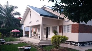 A two-story house with a covered porch, a small garden, and a red umbrella. - Family Nest Kivu Beach (Nyayumba)
