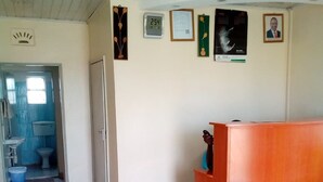 A reception area with a wooden desk, a bench, and a wall with framed pictures and a clock. - Paulice Guest House (Kisumu)