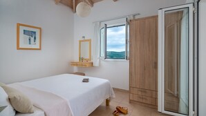 A bedroom with a bed, a bedside table, a mirror, a window with a view, and a wardrobe. - Schiza Houses (Pylos-Nestoras)