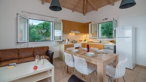 A compact kitchen with wooden cabinets, a dining table with chairs, and a refrigerator. - Schiza Houses (Pylos-Nestoras)