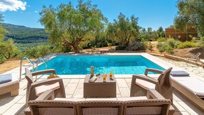 A pool area with wicker furniture, a book, and drinks on a table. - Schiza Houses (Pylos-Nestoras)