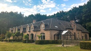 A brick building with multiple gabled roofs and arched windows, surrounded by a well-maintained lawn and hedges. - Guest house beautiful historic square farm 🎯 in Ranst (Broechem Antwerp)
