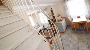Una escalera conduce a una sala de estar con una mesa de comedor y sillas, una cocina con microondas y una estantería.