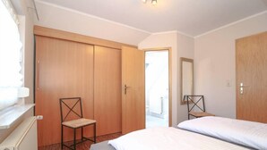 Un dormitorio con dos camas, un armario de madera, una silla y un espejo.