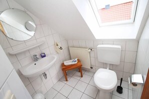 A small, modern bathroom with a skylight, a sink, a toilet, and a small wooden stool. - Huuske een & twee (Krummhoern)