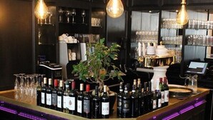 A bar area with a dark wood bar, multiple wine bottles, glasses, and a potted plant. - Hotel Drei Kronen (Lippstadt)