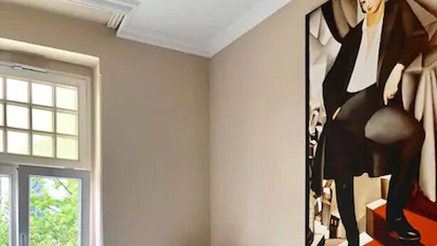 A bedroom with a bed, a window, a radiator, a nightstand with a lamp, and a painting on the wall. - Hotel Drei Kronen (Lippstadt)