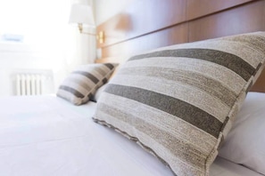 A neatly made bed with striped pillows and a white duvet.