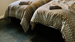 Une chambre d’hôtel avec deux lits, une fenêtre avec des rideaux, un tableau au mur et un lampadaire au plafond.
