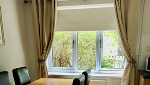 Un coin repas avec une table et des chaises en bois, une fenêtre avec des rideaux et un radiateur.