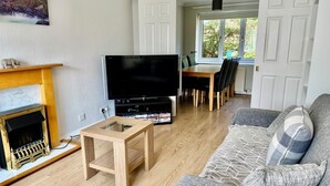Un salon doté d’une cheminée, d’un téléviseur à écran plat, d’une table basse en bois et d’un canapé gris agrémenté de coussins à motifs.
