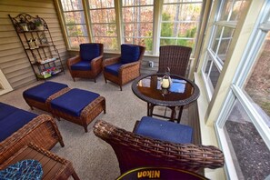 A sunroom with wicker furniture, a glass table with a candle, and a view of trees through large windows. - Forest Landing * 4BR Luxury Resort Home (Frankford)