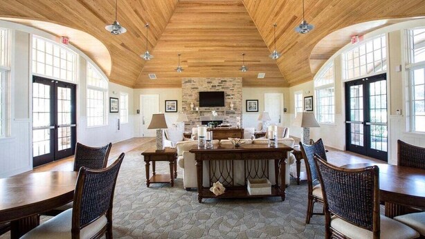 Una habitación amplia con techo de madera alto, chimenea de piedra y una gran mesa de comedor rodeada de sillas.