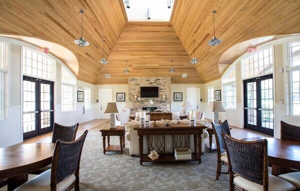 Una habitación amplia con techo de madera alto, chimenea de piedra y una gran mesa de comedor rodeada de sillas.