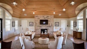 Un salón espacioso con chimenea de piedra, techo de madera y ventanas amplias.