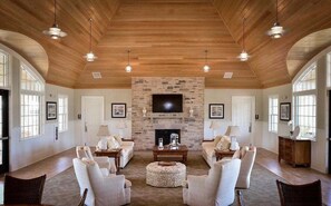 Un salón espacioso con chimenea de piedra, techo de madera y ventanas amplias.