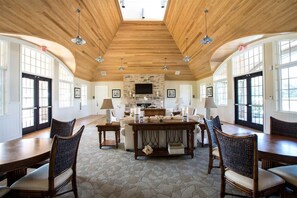 A spacious room with a high wooden ceiling, a stone fireplace, and a large dining table surrounded by chairs. - Forest Landing * 4BR Luxury Resort Home (Frankford)