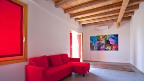 Una habitación con un sofá rojo, un cuadro abstracto grande en la pared y vigas de madera a la vista en el techo.