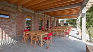 Un patio techado al aire libre con mesas de madera y sillas rojas, paredes de ladrillo y vistas de la vegetación circundante.