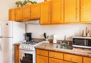 Una cocina con gabinetes de madera, estufa a gas, microondas y refrigerador.