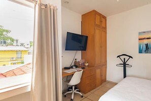 Ein Schlafzimmer mit einem Bett, einem Schreibtisch mit Computer, einem Fernseher und einem Kleiderschrank.
