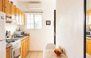 Een kleine keuken met houten kastjes, een gasfornuis, een magnetron en een raam dat voor natuurlijk licht zorgt.