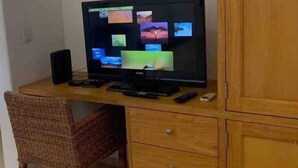 A wooden desk with a flat-screen TV displaying multiple screens, a speaker, and a remote control.